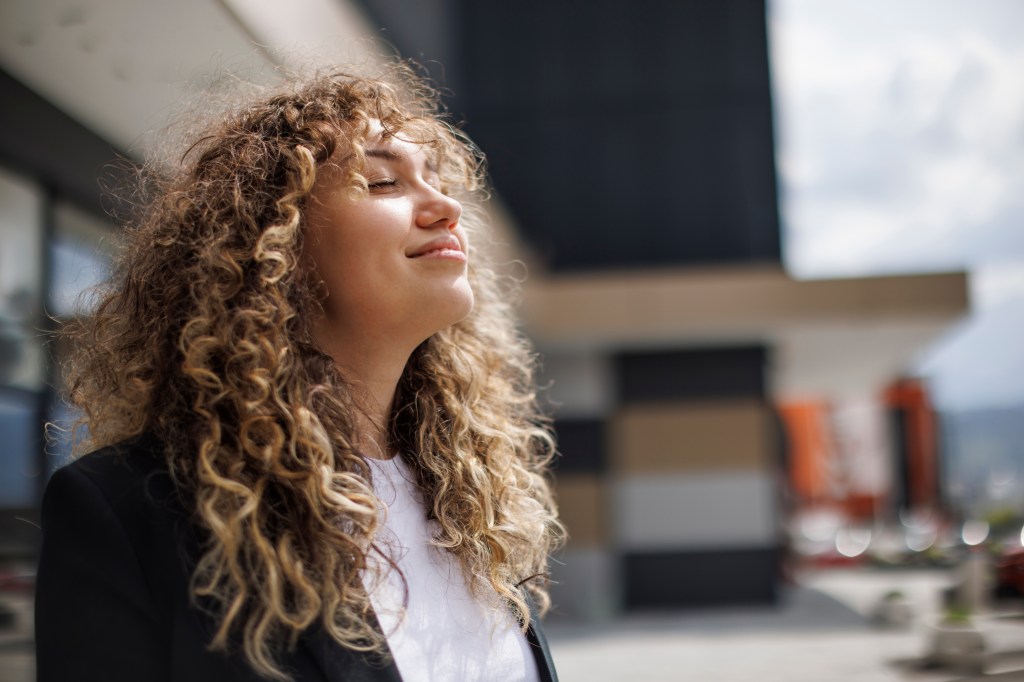 Businesswoman with curly hair relaxing outdoors with closed eyes